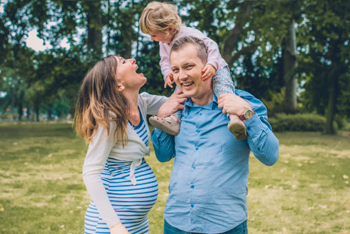 Séance Laetitia, Stéphane et Maëla, photo extérieur Bois de Vincennes, île de Reuilly et Île de Bercy, papa qui porte sa fille sur ses épaules avec maman qui rit